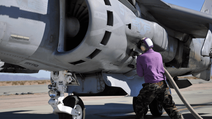 An aviation fuel technician attaches a fuel line to an AV-8B Harrier aircraft