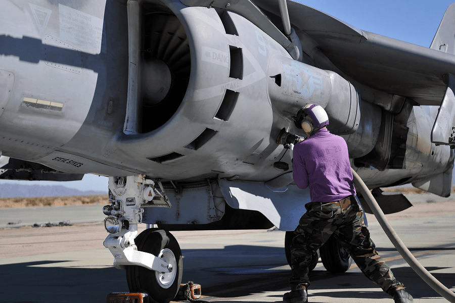 An aviation fuel technician attaches a fuel line to an AV-8B Harrier aircraft
