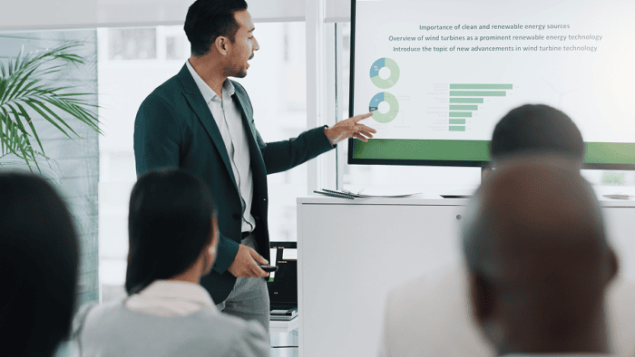 Man in suit jacket pointing at whiteboard screen with graphs