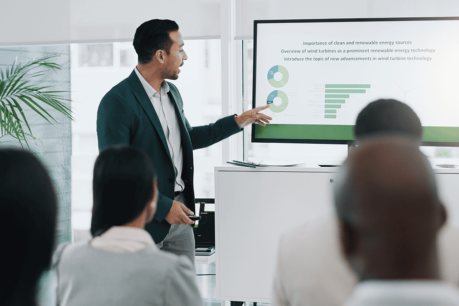 Man in suit jacket pointing at whiteboard screen with graphs
