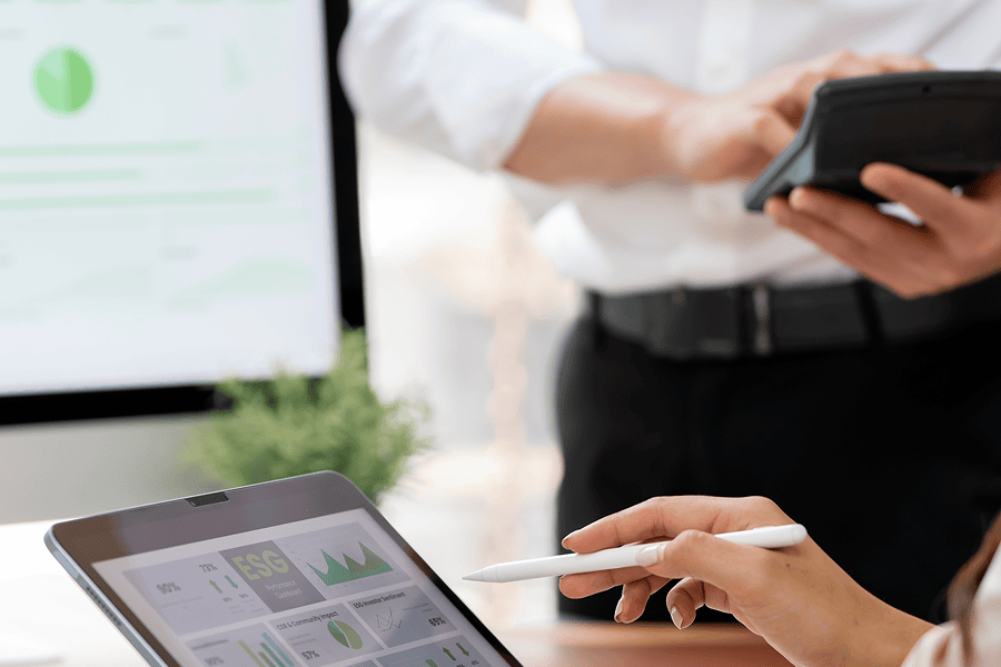 Professionals reviewing ESG performance dashboards and sustainability metrics on digital devices during a business meeting.
