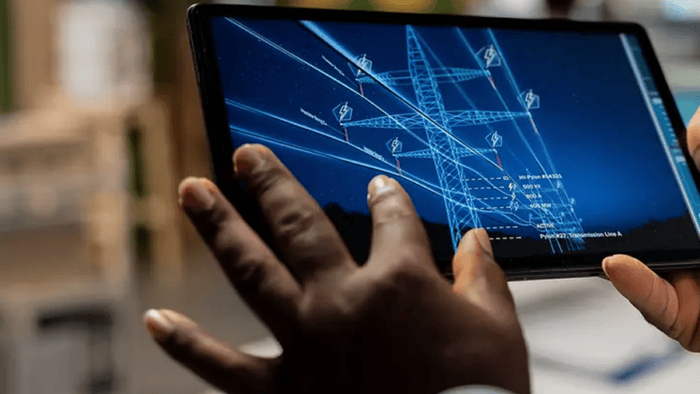Person using a tablet displaying a digital model of an electrical transmission tower and smart grid infrastructure.