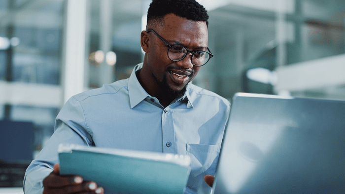 Man working on laptop, holding tablet.