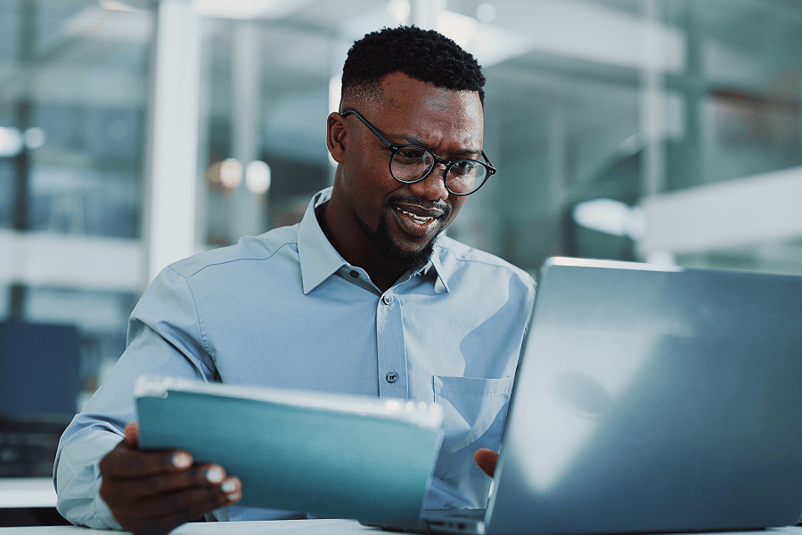 Man working on laptop, holding tablet.