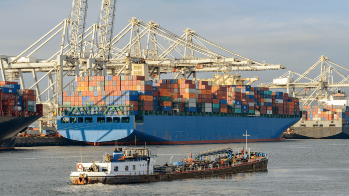 A collection of commercial container ships and a specialized bunker fuel barge operating in a cargo port terminal