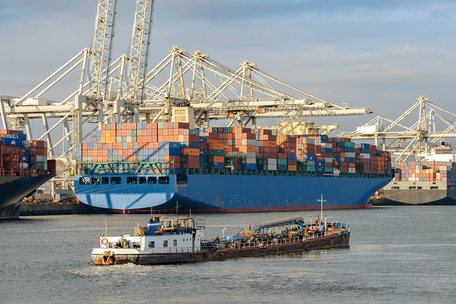 A collection of commercial container ships and a specialized bunker fuel barge operating in a cargo port terminal