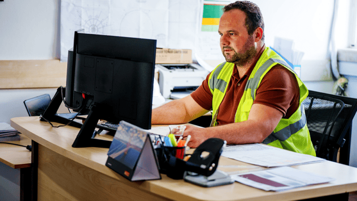 man with safety vest sitting in desk looking at computer screen
