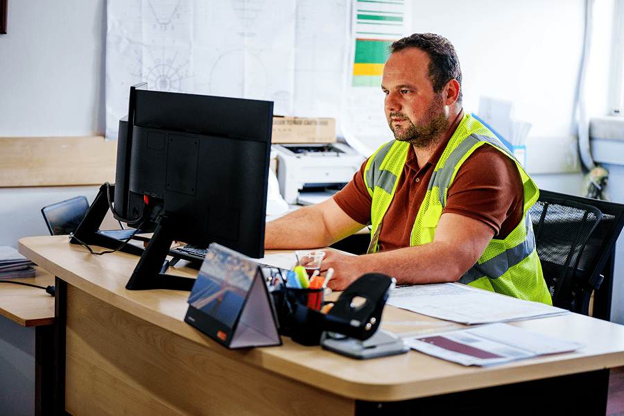 man with safety vest sitting in desk looking at computer screen