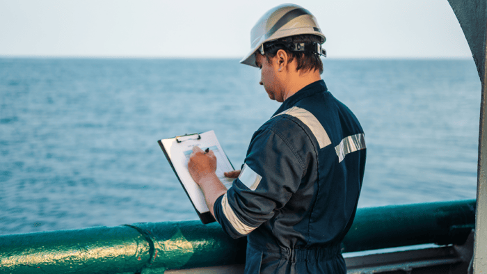 Deck officer wearing PPE completing paperwork at sea