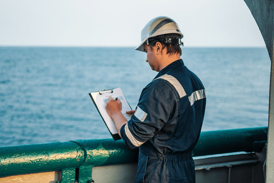 Deck officer wearing PPE completing paperwork at sea