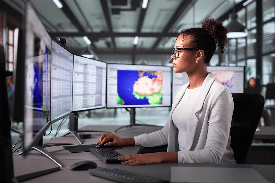 A female logistics coordinator monitoring global vessel routes and real-time transit data across several computer screens in a modern office