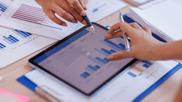 Hands analysing financial graphs on tablet.