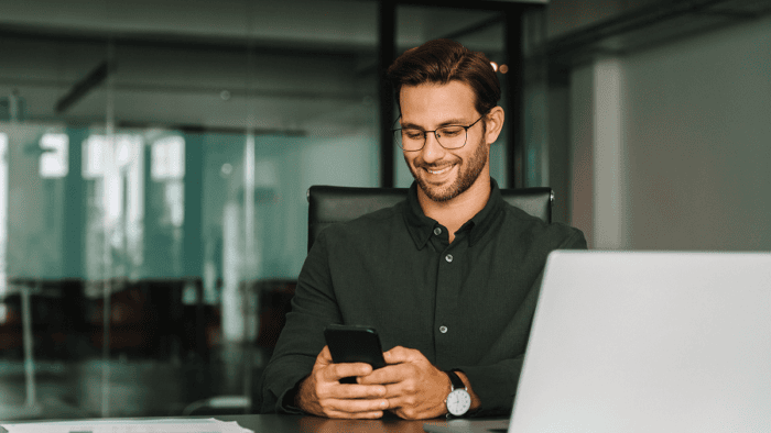 Smiling man using smartphone at desk.