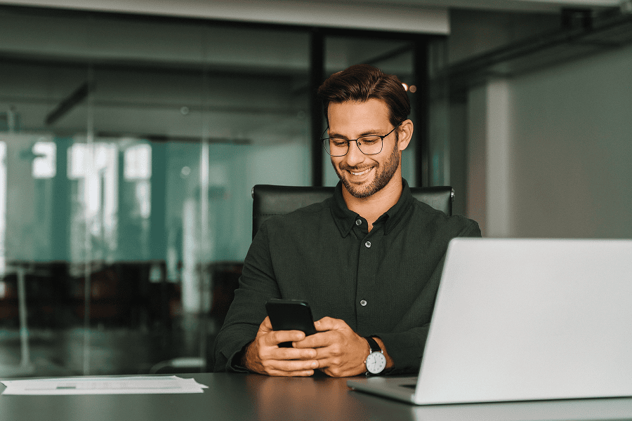 Smiling man using smartphone at desk.