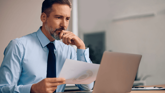 Man analysing reports on laptop thoughtfully.