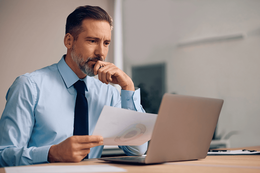 Man analysing reports on laptop thoughtfully.