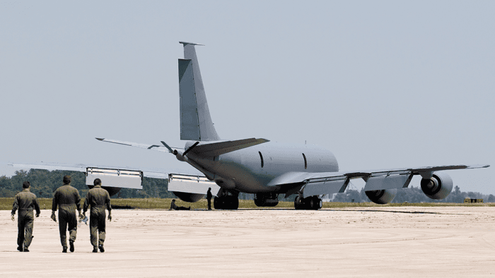 Military tanker aircraft parked on a runway with aircrew walking toward the aircraft.