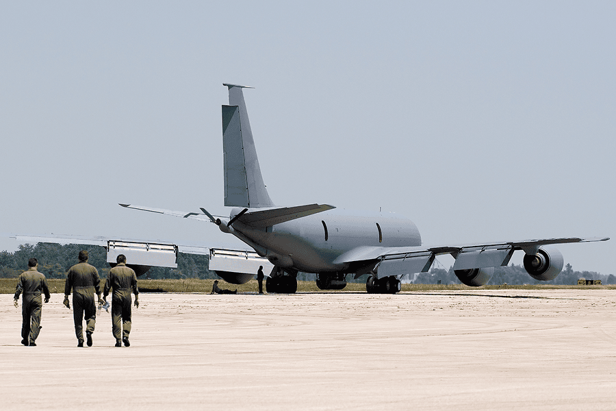 Military tanker aircraft parked on a runway with aircrew walking toward the aircraft.