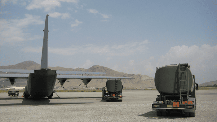 A heavy-duty military fuel tanker truck and cargo defense plane on an airfield tarmac