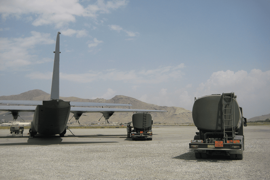 A heavy-duty military fuel tanker truck and cargo defense plane on an airfield tarmac