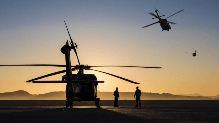 A formation of tactical military helicopters on a mission flying through the sky at sunset