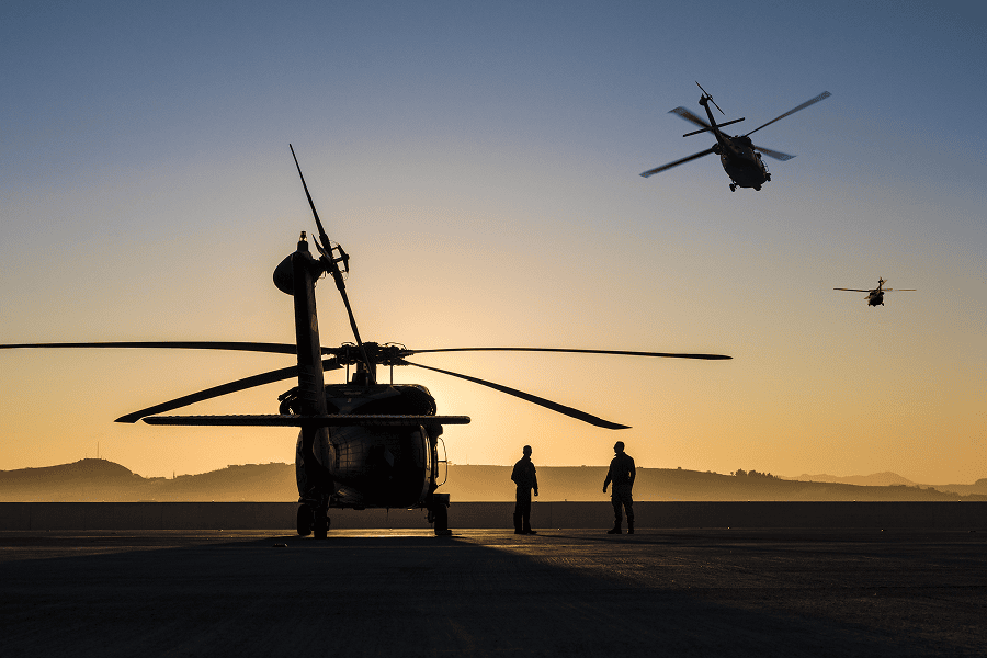 A formation of tactical military helicopters on a mission flying through the sky at sunset