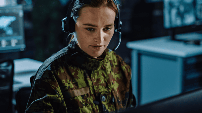 A military soldier in uniform wearing a headset and glancing at a screen