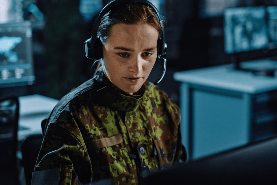 A military soldier in uniform wearing a headset and glancing at a screen
