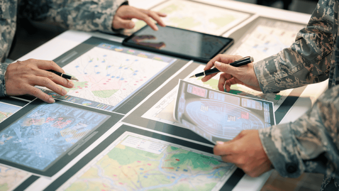 A tactical military team wearing camouflage uniforms studies topographic maps