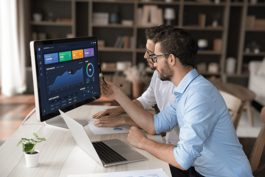 two guys at desk with market related data on screen