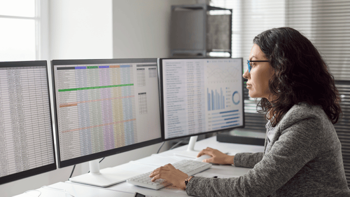 Professional monitoring operational data and analytics dashboards across multiple computer screens in an office setting.