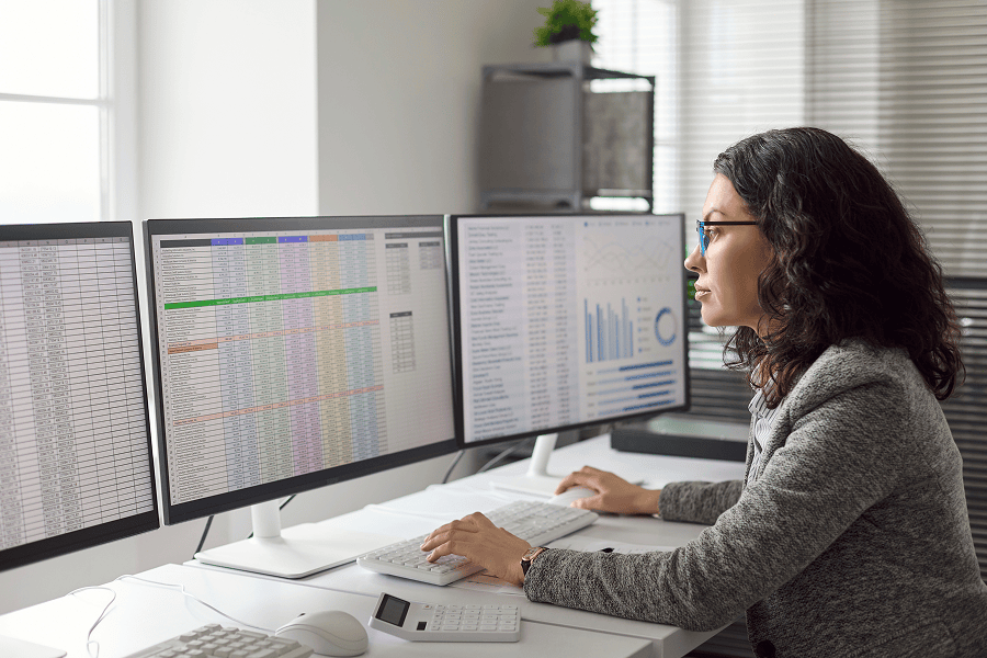 Professional monitoring operational data and analytics dashboards across multiple computer screens in an office setting.