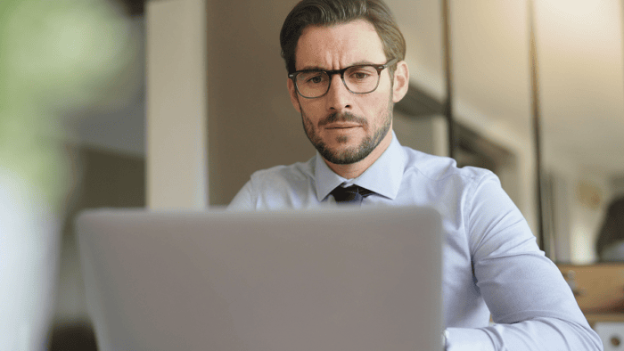 A young businessman in a modern office looking at a laptop screen