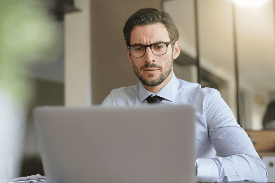 A young businessman in a modern office looking at a laptop screen